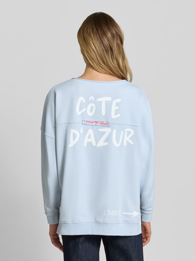 Frauenmodel trägt Oversized Sweatshirt mit Statement-Print und Rollsaum von Smith and Soul, hellblauer Baumwoll-Mix mit Modal-Anteil, Rundhalsausschnitt, überschnittene Schultern, Motiv-Print, Rollsaum, Ganzkörperansicht Rückansicht.