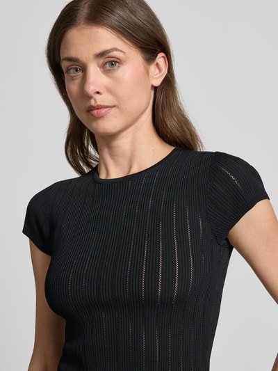Frauenmodel trägt T-Shirt in Pointelle-Optik mit Rundhalsausschnitt von Guess aus Viskose-Mix, schwarzer Farbton, körpernaher Schnitt, Nahaufnahme Oberkörper.