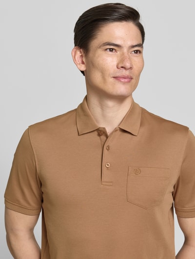 Männermodel trägt Regular Fit Poloshirt mit Brusttasche und Label-Stitching von bugatti in Beige mit Polokragen, Knopfleiste, Nahaufnahme Oberkörper. Rückenlänge bei Größe M: 70 cm.