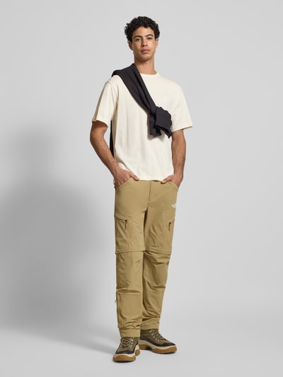 Männermodel trägt T-Shirt mit Label-Print von The North Face aus reiner Baumwolle, Regular-Fit, gerippter Rundhalsausschnitt, Vorderansicht Ganzkörperansicht. Rückenlänge bei Größe M: 69 cm.