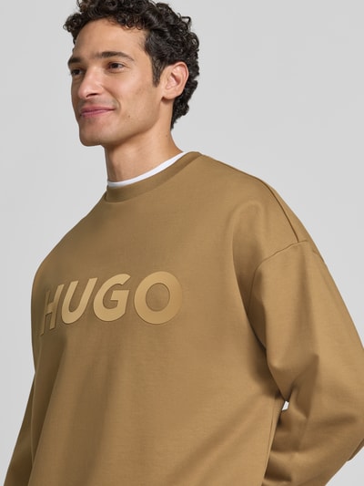 Männermodel trägt Regular Fit Sweatshirt aus reiner Baumwolle Modell 'Dinex' von HUGO in Braun mit HUGO-Logo, Nahaufnahme Oberkörper. Herren Sweatshirt von HUGO.