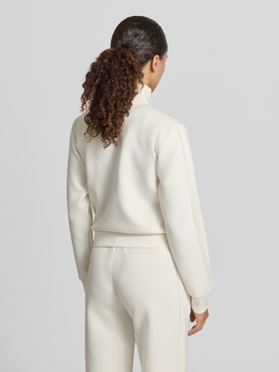 Frauenmodel trägt Sweatjacke mit Logo-Muster Modell 'CALISTA' von Guess Activewear, cremefarben, strukturierter Stoff, Ganzkörperansicht Rückansicht.
