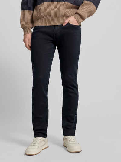 Męski model nosi Tapered Fit Jeans mit Label-Detail Modell 'Lyon' od Pierre Cardin, mieszanka bawełny z dodatkiem streczu, ciemnoniebieski kolor, widoczne logo, szerokość w pasie 39 cm, długość wewnętrzna nogawki 79 cm, Ganzkörperansicht z przodu.