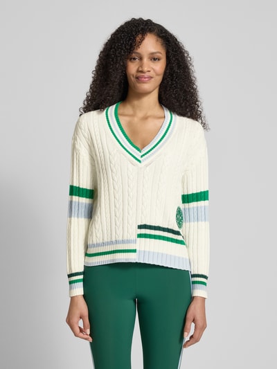 Frauenmodel trägt Relaxed Fit Pullover mit Lanawoll-Anteil von Marc Cain, Baumwoll-Mix, V-Ausschnitt, weiß mit grünen und blauen Streifen, Logo-Stitching auf Hüfthöhe, strukturierte Oberfläche, Ganzkörperansicht von vorne.