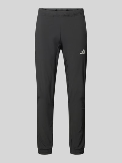 Produktfoto, schwarze Regular Fit Trackpants mit elastischem Logo-Bund von adidas Training, unifarben, seitliche Reißverschlusstaschen, schnelltrocknend, schweißableitend, elastischer Bund und Beinabschluss.