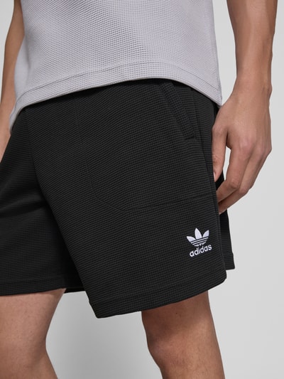 Männermodel trägt Relaxed Fit Sweatshorts mit Baumwoll-Anteil von adidas Originals, unifarben schwarz, Waffelstruktur, Nahaufnahme Oberschenkel.