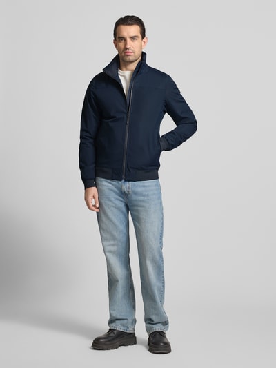 Męski model nosi Regular Fit Kurtka z stójką Model 'Alvin' od Didriksons, zamek błyskawiczny, elastyczne wykończenia, wpuszczane kieszenie, długość tyłu w rozmiarze M: 69 cm, szerokość ramion w rozmiarze M: 44 cm, szerokość w rozmiarze M: 54 cm, długość rękawów w rozmiarze M: 70 cm, kolor granatowy, gładka faktura, całkowity widok z przodu