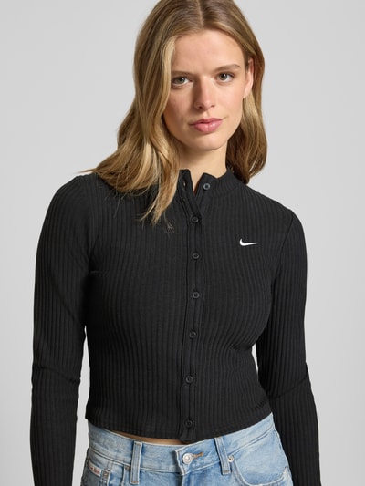 Frauenmodel trägt Cardigan in Ripp-Optik Modell 'CHILL' von Nike in Schwarz mit Stehkragen, Skinny Fit und Knopfleiste, Nahaufnahme Oberkörper.