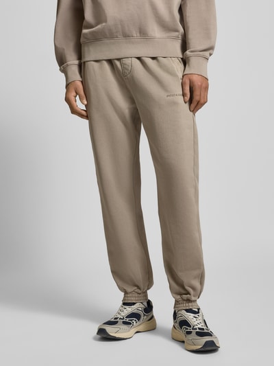 Männermodel trägt Sweatpants mit elastischem Bund van Pegador, katoenmix, losse pasvorm, Franse zakken, label-stitching, beige tint, Nahaufnahme onderlichaam.