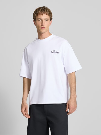 Męski model nosi T-Shirt mit Logo- und Statement-Print od REVIEW, czysta bawełna, krój loose fit, biały, okrągły dekolt, widok z przodu pełnej sylwetki.