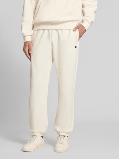 Männermodel trägt Sweatpants mit Label-Detail von Champion in Beige, gerade Form, Baumwollmischung, Nahaufnahme Unterkörper.