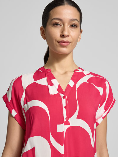 Frauenmodel trägt Regular Fit Bluse aus reiner Viskose Modell 'Miriama' von ZABAIONE in Pink mit abstrakten weißen Formen, Kurzarm, Tunika-Ausschnitt, elastischer Bund, Rückenlänge bei Größe S: 62 cm, Nahaufnahme Oberkörper.