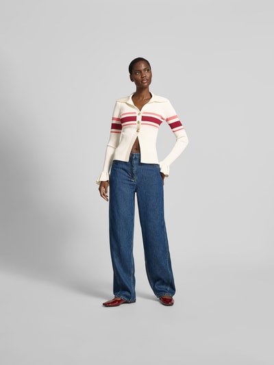 Frauenmodel trägt Strickjacke aus Viskose-Mix von Self-Portrait in Creme mit roten Streifen, eng anliegend, Knopfleiste, Jeans, Ganzkörperansicht von vorne.
