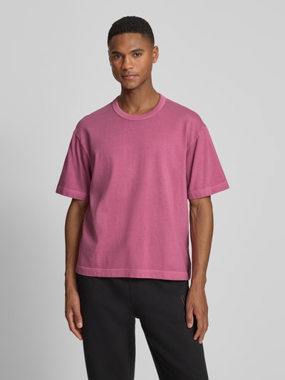Männermodel trägt Cropped T-Shirt mit Rundhalsausschnitt von GAP in Pink, reine Baumwolle, lockere Passform, Ganzkörperansicht von vorne.