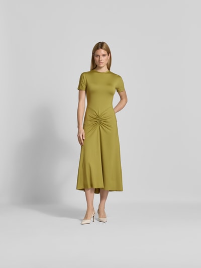 Frauenmodel trägt Midikleid mit Raffungen von Victoria Beckham in Olivgrün, taillierte Passform, elastischer Stoff, Ganzkörperansicht von vorne.