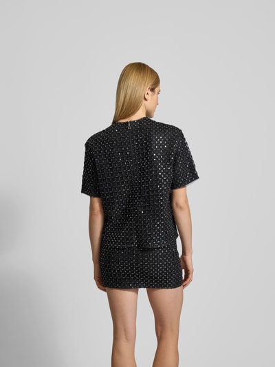 Frauenmodel trägt Oversized T-Shirt mit Ziersteinen von ROTATE, Allover-Pailettenbesatz, Rundhalsausschnitt, Kurzärmelig, Rückenlänge 59 cm, Ganzkörperansicht Rückansicht.