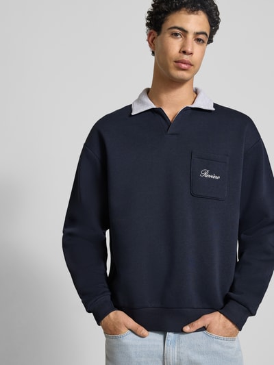 Mannenmodel draagt Sweatshirt mit Kontrastkragen und Brusttasche mit Logo-Bestickung van REVIEW, Materiaalmix met katoen, regular fit, contrastkraag, borstzak met geborduurd logo, ruglengte maat M 71 cm, mouwlengte maat M 63 cm, donkerblauw met lichtgrijze kraag, gladde textuur, Nahaufnahme bovenlichaam.