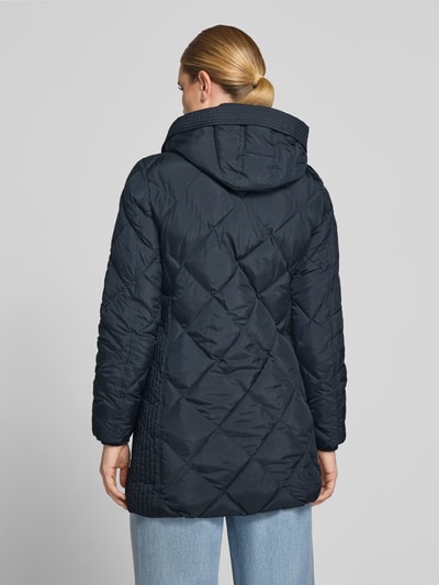 Frauenmodel trägt Regular Fit Mantel in Stepp-Optik von FUCHS SCHMITT in dunklem Blau mit Kapuze, Ganzkörperansicht Rückansicht. Mantel mit Stehkragen, Eingrifftaschen, Rücklänge ca. 84 cm, Schulterbreite ca. 42 cm, Brustweite ca. 47 cm, Ärmel ca. 64 cm.