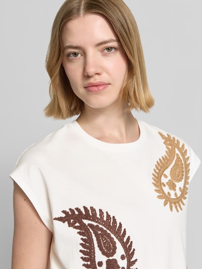 Frauenmodel trägt T-Shirt mit Rundhalsausschnitt und Stitchings Modell 'RICAMO' von Stefanel aus reiner Baumwolle, Regular Fit, weiße Grundfarbe mit braunen Paisley-Details, Nahaufnahme Oberkörper.