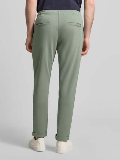 Mężczyznamodel nosi Regular Fit Hose mit elastischem Bund od Antony Morato, mieszanka bawełny, pionowe szwy, elastyczny pas, szerokość w rozmiarze M 41 cm, długość wewnętrzna nogawki w rozmiarze M 76 cm, zielony kolor, gładka tekstura, spodnie męskie, widok całej sylwetki z tyłu