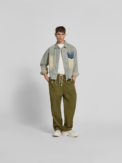 Männermodel trägt Balloon Fit Stoffhose aus Baumwolle von Officine Générale in Olivgrün mit elastischem Bund, Ganzkörperansicht von vorne.