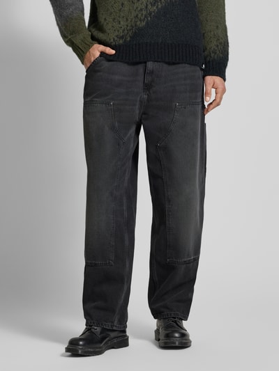 Männermodel trägt Wide Fit Jeans Logo-Patch Modell 'Grind' von Carhartt Work In Progress, schwarze Reine Baumwolle, 5-Pocket-Design, Knopf-Reißverschluss, Ganzkörperansicht von vorne.