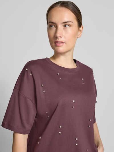 Frauenmodel trägt T-Shirt aus reiner Baumwolle von Christian Berg Woman in Lila mit Ziersteinen und lockerer Passform, Nahaufnahme Oberkörper. Rückenlänge bei Größe S: 57 cm, überschnittene Schultern.