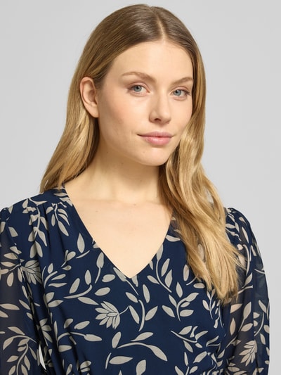 Kobiece modelka nosi Knielanges Kleid mit Kordelzug an der Taille von Apricot w granatowym kolorze z beżowym wzorem liści, dekolt w serek, rękaw o dł. 1/2 z elastycznym zakończeniem, taliowany, tkanina lekko prześwitująca, detal kontekst: długość do kolan, szerokość w rozmiarze S: 43 cm, długość tyłu w rozmiarze S: 93 cm, długość rękawów w rozmiarze S: 30 cm, dół obszyty falbaną, Nahaufnahme górnej części ciała.