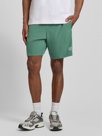 Männermodel trägt Shorts mit elastischem Bund und Logo von EA7 Emporio Armani in Grün, Regular Fit, Nahaufnahme Unterkörper.