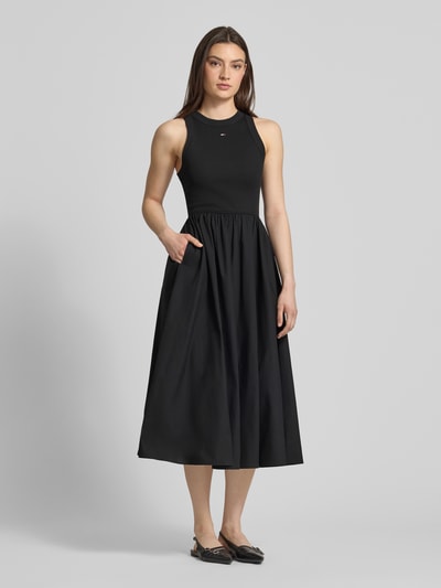 Frauenmodel trägt Midikleid aus reiner Baumwolle von Tommy Jeans in Schwarz, ärmellos, A-Linie, unifarben, Ganzkörperansicht von vorne.