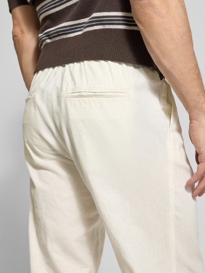 Männermodel trägt Straight Fit Leinenhose mit elastischem Bund Modell 'Barton' von Matinique, mieszanka lnu i bawełny, krój straight fit, elastyczny pas z tunelem, kieszenie z tyłu, szerokość w rozmiarze M 34 cm, długość wewnętrzna nogawki 78 cm, jasny kolor, gładka tekstura, zdjęcie z tyłu, detal pasa i kieszeni, zbliżenie