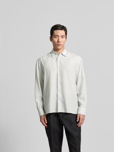 Männermodel trägt Freizeithemd aus Lyocell-Mix von Officine Générale, weiß mit feinen grünen Streifen, Kentkragen, lange Ärmel, Ganzkörperansicht von vorne.