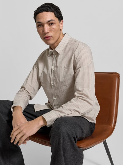 Männermodel trägt Slim Fit Freizeithemd aus Baumwoll-Mix von MAISON KITSUNÉ in Beige mit feinen Streifen, Knopfleiste, Kentkragen, Langarm, Nahaufnahme Oberkörper.