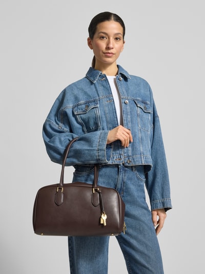 Frauenmodel trägt Handtasche mit Tragehenkeln Modell 'CADIZ' von Mango, braun, glatte Oberfläche, Innenfach mit Reißverschluss, Ganzkörperansicht von vorne.