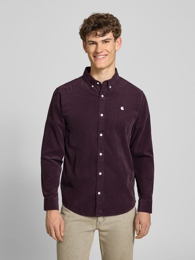 Mężczyzna model nosi Regular Fit Freizeithemd aus Cord mit Button-Down-Kragen od Carhartt Work In Progress, kolor ciemnofioletowy, czysta bawełna, label-stitching, krój regular fit, koszula model Madison, całkowita długość z przodu.
