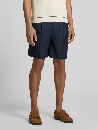 Mężczyzna nosi Loose Fit bermudy z dodatkiem wełny model 'OTTO' od SELECTED HOMME, efekt: jednolity kolor, zakładki w pasie, szlufki na pasek, wpuszczane kieszenie, kieszenie z wypustkami, zapięcie na guzik i ukryty zamek błyskawiczny, widok na nogi i spodnie, detal, szorty w kolorze granatowym, całkowity widok z przodu.
