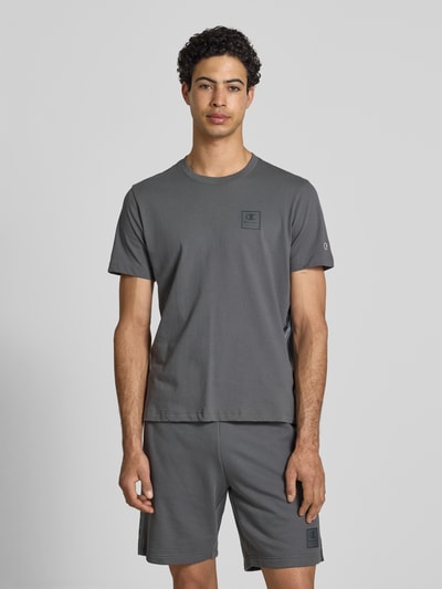 Männermodel trägt T-Shirt mit Logo und Rundhalsausschnitt von CHAMPION in Grau, reine Baumwolle, Regular Fit, Ganzkörperansicht von vorne.