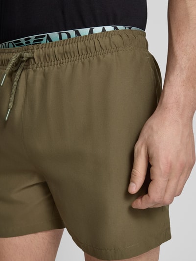 Männermodel trägt Relaxed Fit Badeshorts mit Logo-Stitching von Emporio Armani in Olive mit elastischem Bund und Tunnelzug, Nahaufnahme Oberkörper.