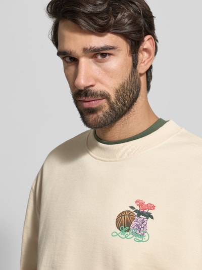 Męski model nosi Sweatshirt mit Label-Print und Rundhalsausschnitt od Les Deux z czystej bawełny, kremowy kolor, nadruk, ujęcie: zbliżenie na górną część ciała.