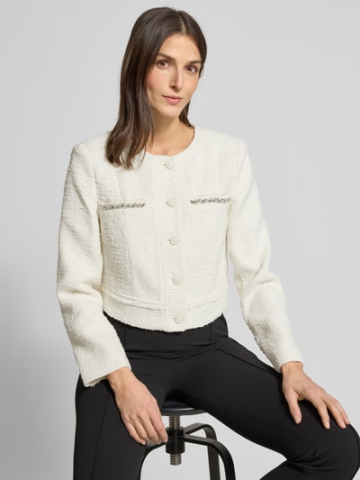 Kobiece model prezentuje Regular Fit Żakiet z mieszanki wełny lana model 'Clotilde' od Guess, okrągły dekolt, listwa guzikowa, obszycie ozdobnymi kamieniami, biały, faktura boucle, długość tyłu 44 cm, szerokość klatki piersiowej 46 cm, długość rękawów 62 cm, widok na górną część ciała z przodu.