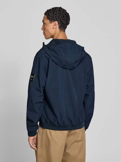 Männermodel trägt Regular Fit Jacke mit Logo-Detail von JACK & JONES, dunkelblau, Softshell, Kapuze, elastische Abschlüsse, Ganzkörperansicht Rückansicht.