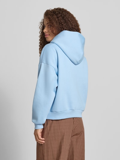 Frauenmodel trägt Hoodie mit Logo-Print und Känguru-Tasche von REVIEW, hellblauer Baumwoll-Mix, Loose-Fit, Kapuze, Ganzkörperansicht Rückansicht.