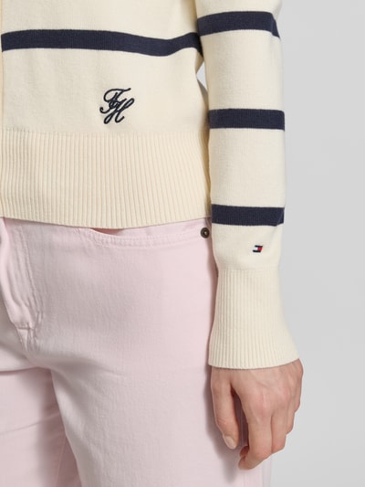Frauenmodel trägt Regular Fit Strickjacke aus reiner Baumwolle von Tommy Hilfiger, Optik:Allover-Muster, gestreift, Logo-Stitching, Regular-Fit, einreihige Knopfleiste, Rundhals, Langarm, Feinstrick, Creme mit navy Streifen, feine Textur, Gerippt an Ärmelabschluss und Rumpfabschluss, Nahaufnahme Oberkörper.