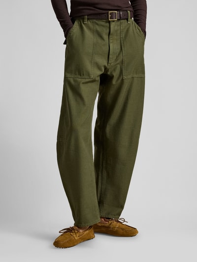 Männermodel trägt Tapered Stoffhose aus reiner Baumwolle von Polo Ralph Lauren, oliwkowy kolor, wysoki stan, krój tapered, naszywane kieszenie, widok całej sylwetki z przodu.