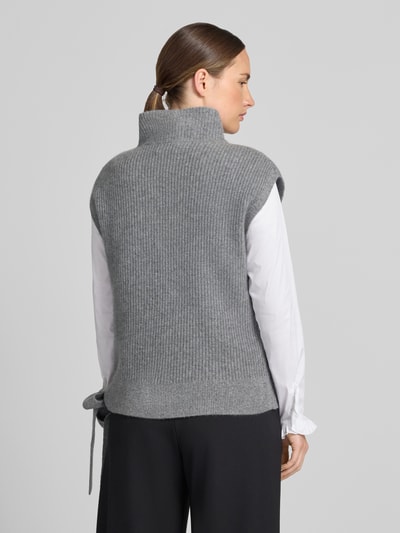 Frauenmodel trägt Relaxed Fit Pullunder aus reinem Kaschmir mit Stehkragen von Christian Berg Woman in Grau, Zierschleife am Saum, Ganzkörperansicht Rückansicht.