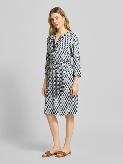 Frauenmodel trägt Regular Fit Midikleid aus reiner Viskose von Betty Barclay mit Tunika-Ausschnitt, Taillierter Passform, 7/8-Arm, Abnehmbarem Stoffband, geometrischem Allover-Print, Rückenlänge 99 cm, Brustweite 40 cm, Ärmellänge 47 cm, Ganzkörperansicht von vorne.