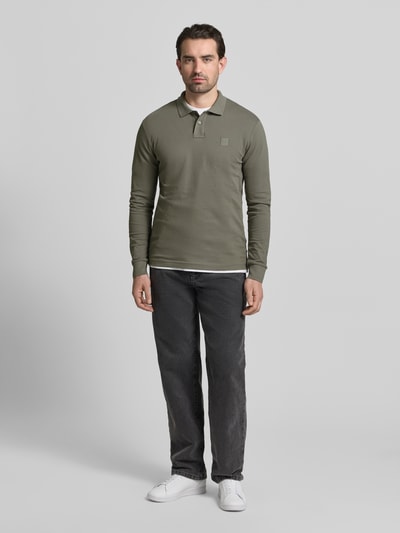 Männermodel trägt Slim Fit Poloshirt aus Baumwoll-Mix Modell 'PASSERBY' von BOSS Orange in Olivgrün, unifarben, Piqué, Ganzkörperansicht von vorne.