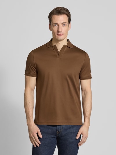 Männermodel trägt Regular Fit Poloshirt aus reiner Baumwolle von Tommy Hilfiger, braun, unifarben, Logo-Detail, Ganzkörperansicht von vorne.
