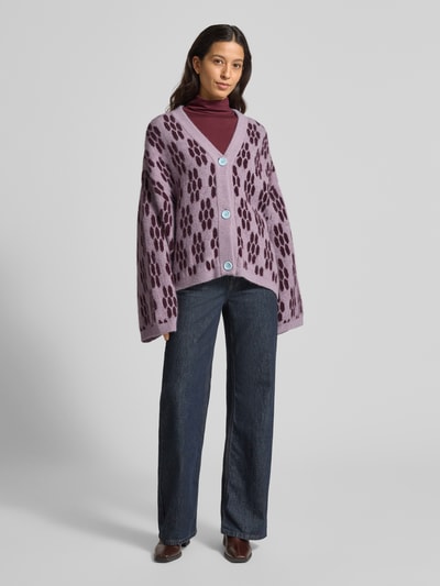 Vrouwenmodel draagt Gebreid jack met knoopsluiting Model 'VITOW' van American Vintage, mix van alpaca en lanawol met stretch, los model, ribboorden, V-hals, paarse tinten en donker patroon, voor dames, confectiemaat XS/S, ruglengte 67 cm, mouwlengte 53 cm. Ganzkörperansicht von vorne.