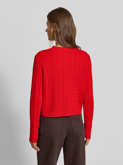 Frauenmodel trägt Strickjacke mit Woll-Anteil von MYON in Rot mit Zopfmuster, gerippten Abschlüssen, gerade Passform, Ganzkörperansicht Rückansicht.